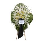 تاج گل ترحیم طبیعی با گلهای لیلیوم سفید و زرد، گلایل سفید و برگهای تزئینی سبز تازه، روبان مشکی و پایه چوبی، مناسب مراسم ختم و تسلیت